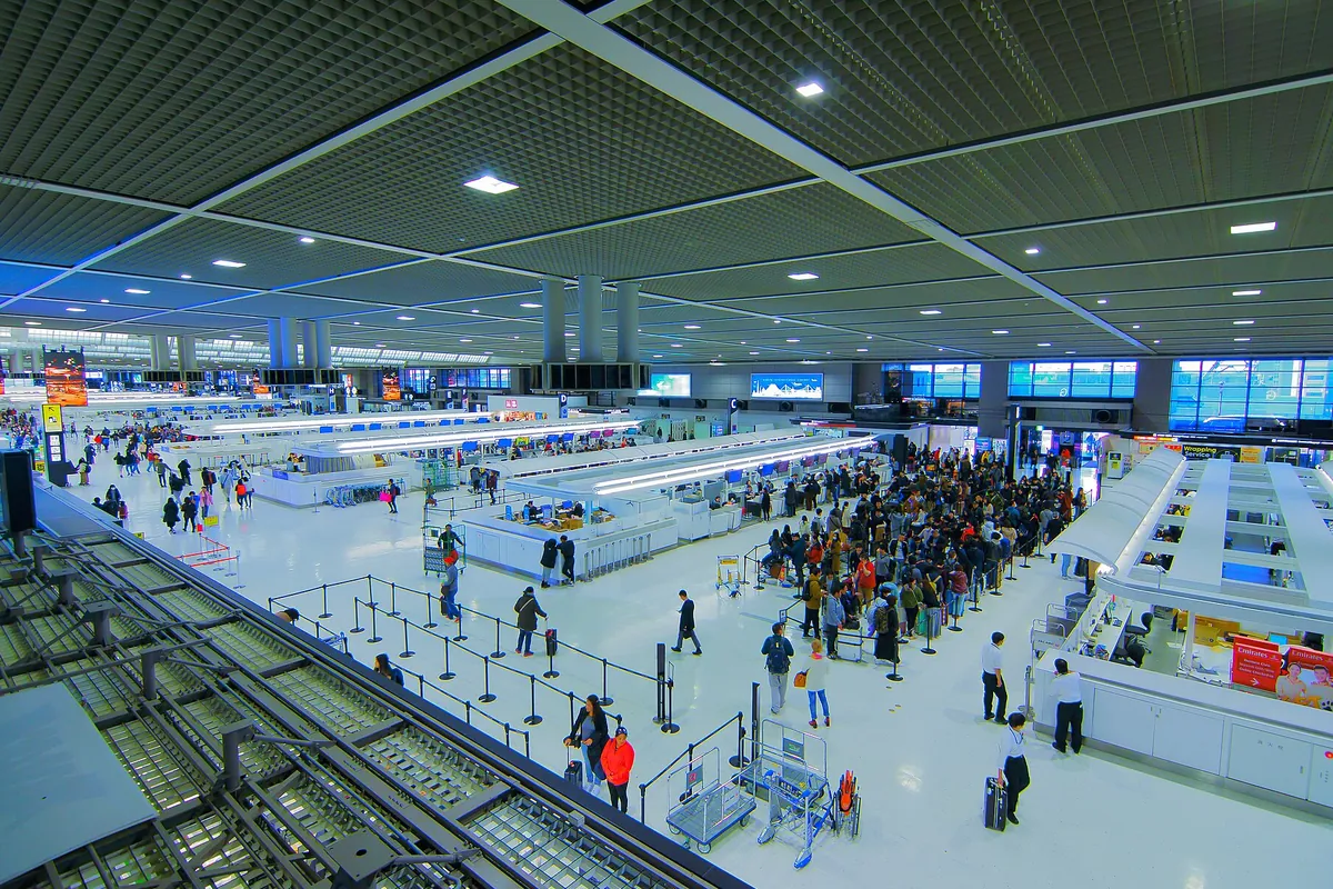 空港の出発ロビーで、多くの利用客が列をつくりカウンター前に並んでいる様子の写真