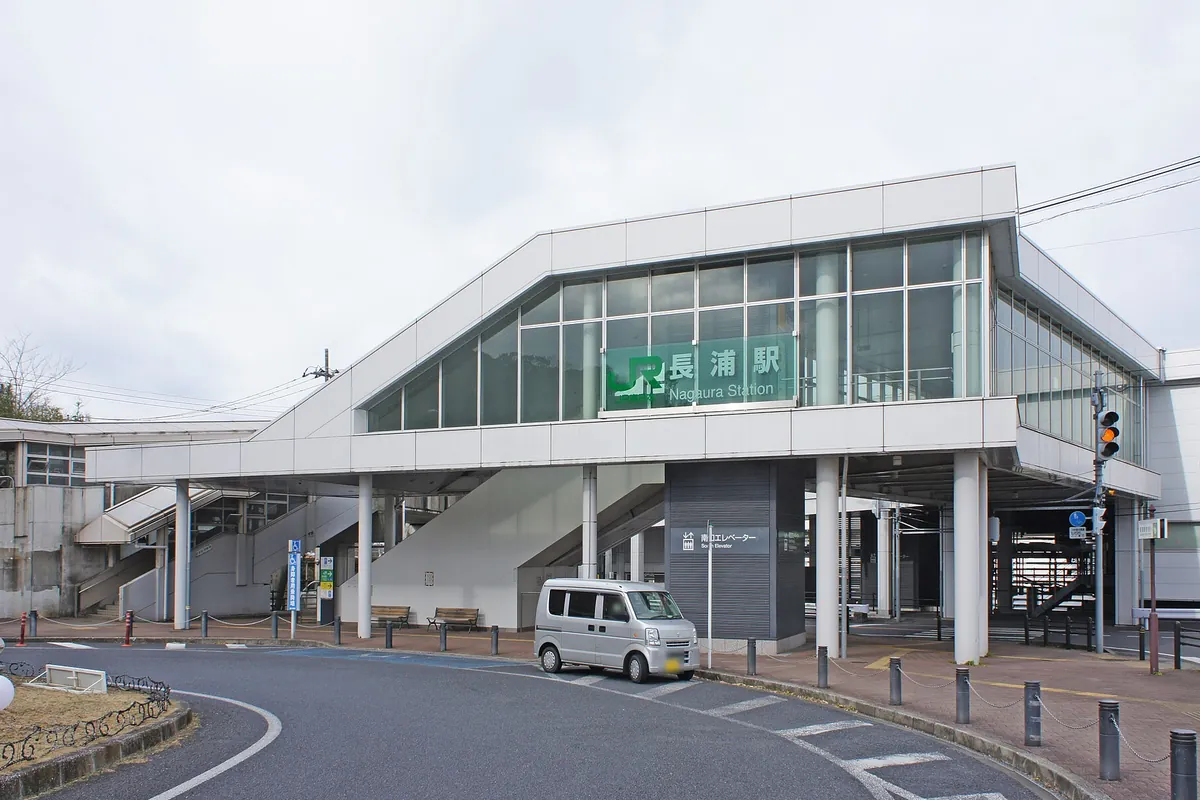「長浦駅」の看板が掲げられたJR長浦駅の駅舎前にロータリーと軽自動車が停まっている様子の写真