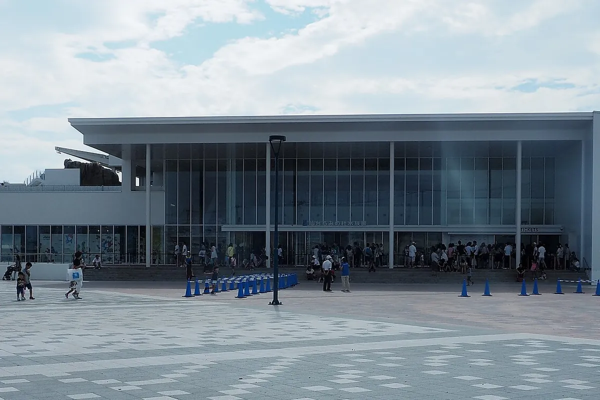 仙台うみの杜水族館の建物外観で、入口付近に並ぶ来場者とガラス張りの大きな屋根が写った写真