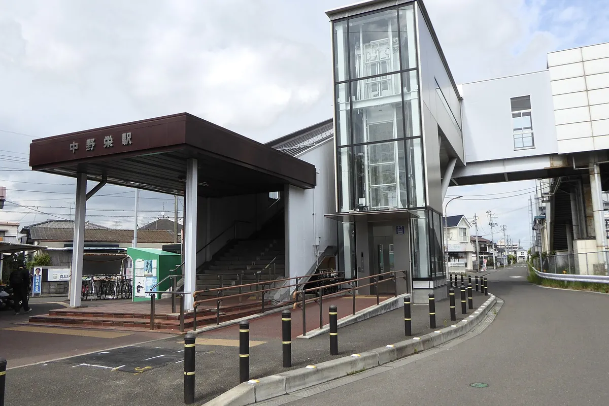 「中野栄駅」と書かれた駅舎の入口に屋根付きの階段とエレベーターが並ぶ様子の写真