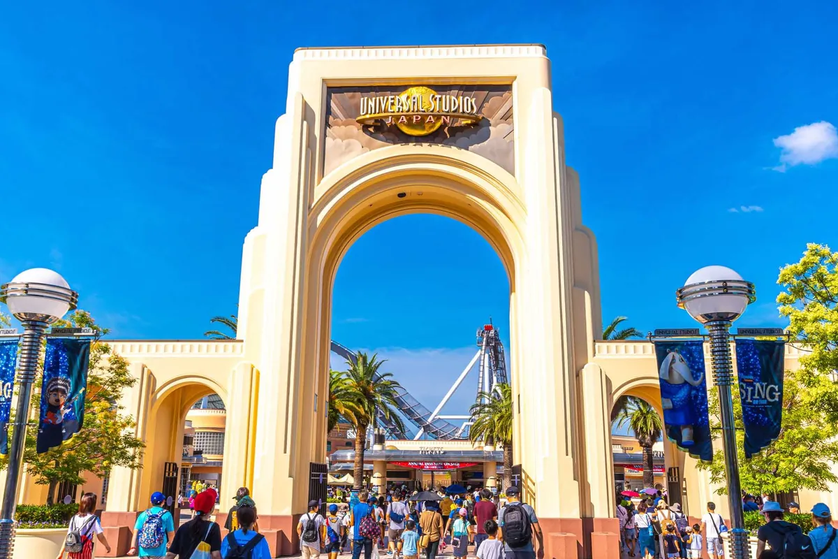「UNIVERSAL STUDIOS JAPAN」の文字がある入口ゲートのアーチをくぐって来場者が歩いている様子の写真