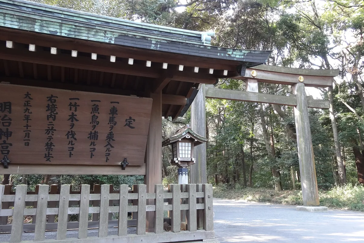 明治神宮の木造の大鳥居と、その手前に「定」と書かれた高札と灯籠が立つ参道の様子の写真
