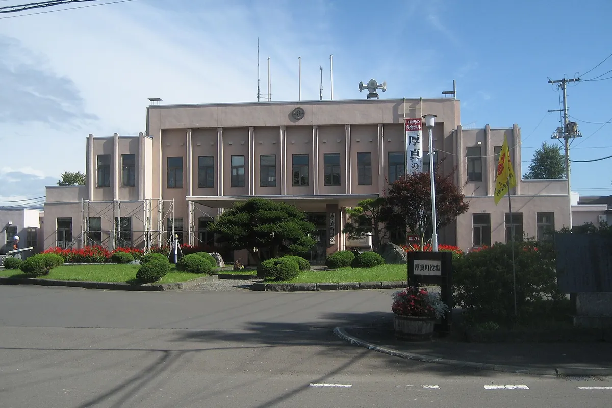 北海道の町役場と見られる洋風の建物と前庭の植え込み、「厚真町役場」と書かれた看板が立つ様子の写真