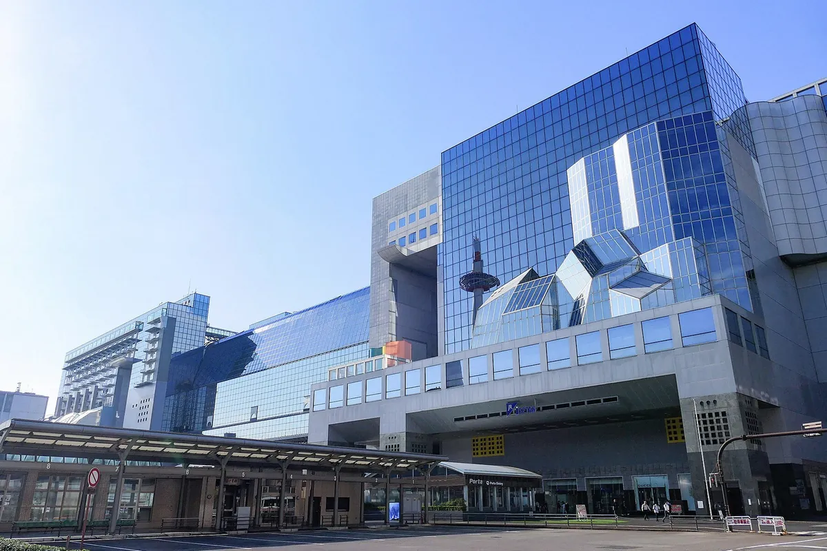 京都駅ビルのガラス張りの外観と空中経路、京都タワーの先端が映り込んだ建物の写真