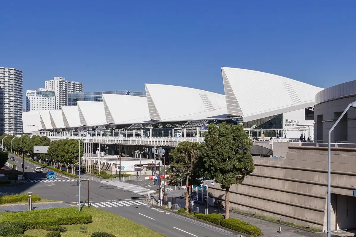 パシフィコ横浜（会場）の展示ホールで、白い帆のような屋根が連なる建物と、手前の道路や植え込みの写真