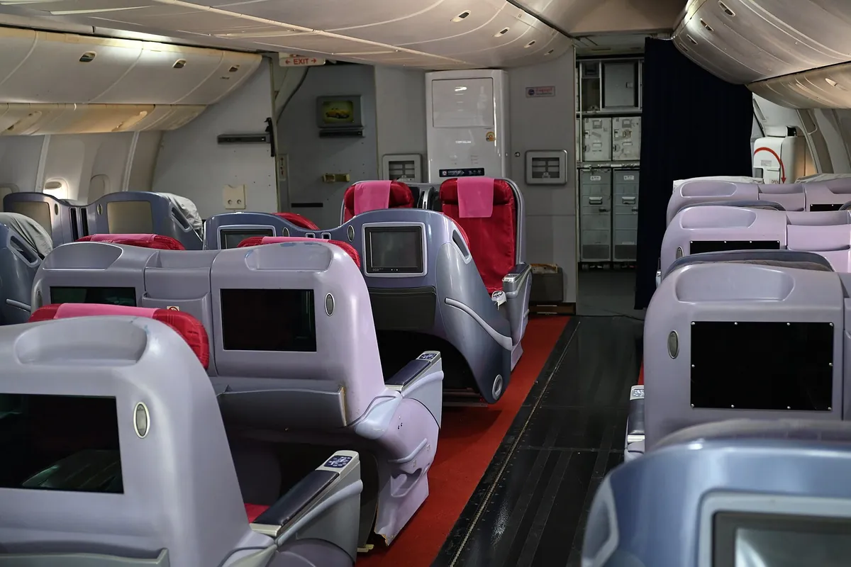 飛行機の機内で、灰色のシートが並び各座席にモニターが設置されたキャビンの様子の写真